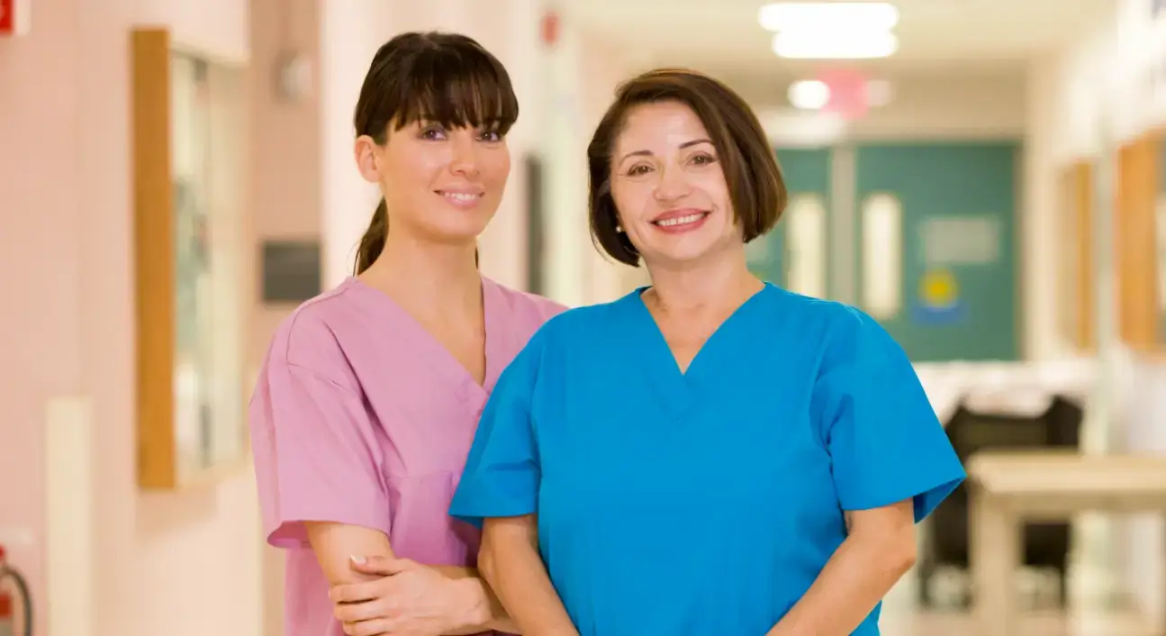 Two nurses smiling in a hospital hallway.