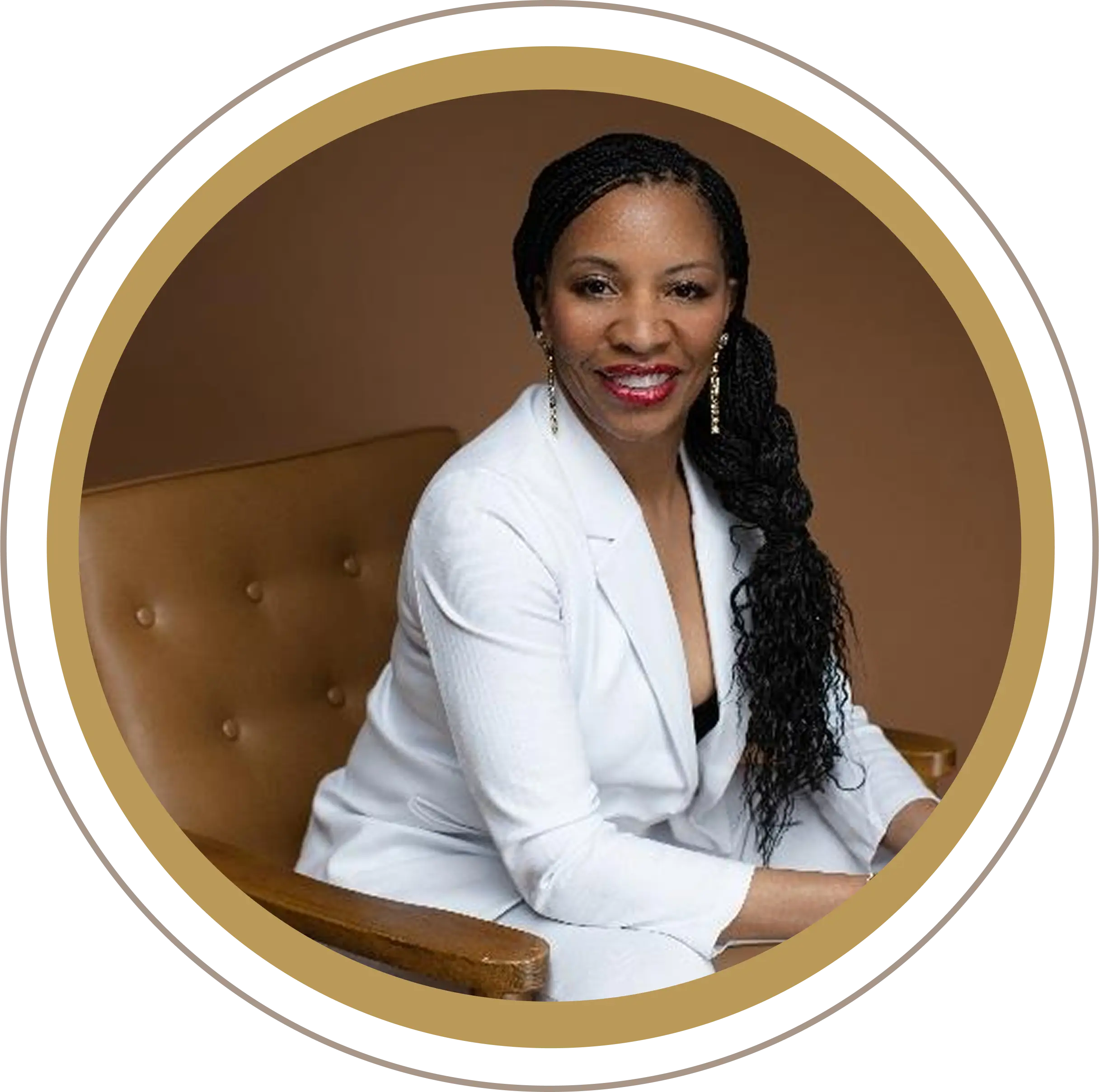 Confident woman in white suit sitting on a brown chair, smiling warmly.