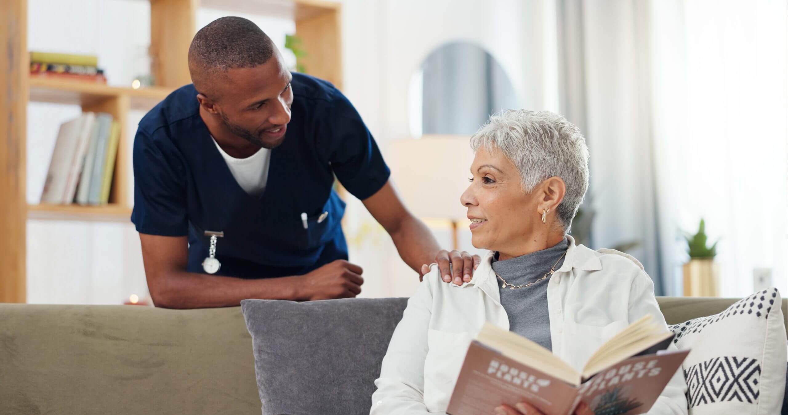 A nurse warmly interacts with an elderly woman holding a book.